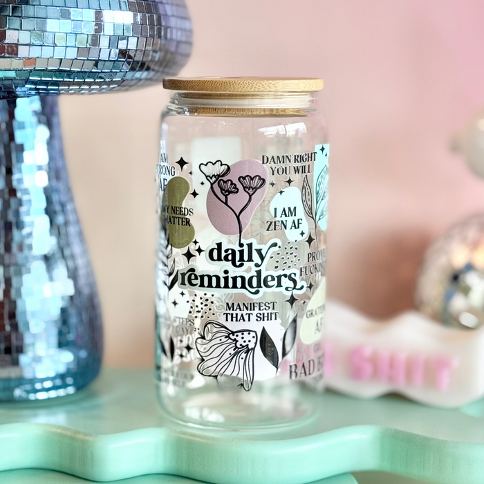 Glass jar with decorative text and illustrations on a light blue stand with a pink background