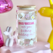 Jar with text on a pink stand with decorative items in the background