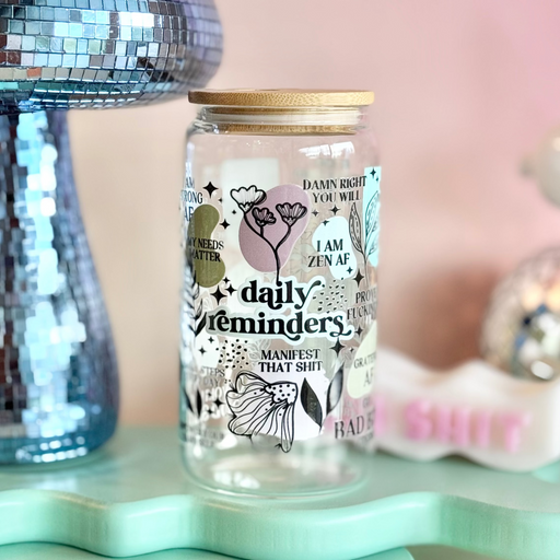 Glass jar with decorative text and illustrations on a light blue stand with a pink background