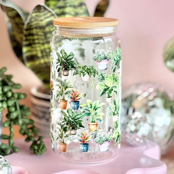 Decorative glass jar with plants on a pink stand, surrounded by festive decorations.