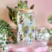 Decorative jar with plant designs on a pink stand against a pink wall with festive decorations.