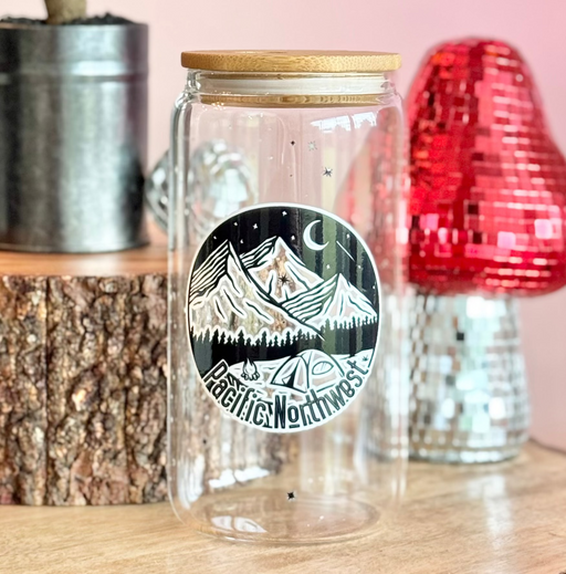 Clear glass jar with mountain design on a wooden surface with decorative items.