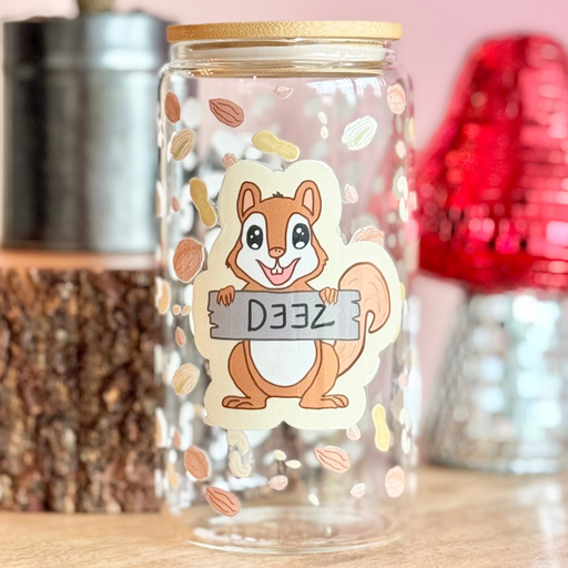 Decorative glass jar with a squirrel design on a wooden surface with a pink background.